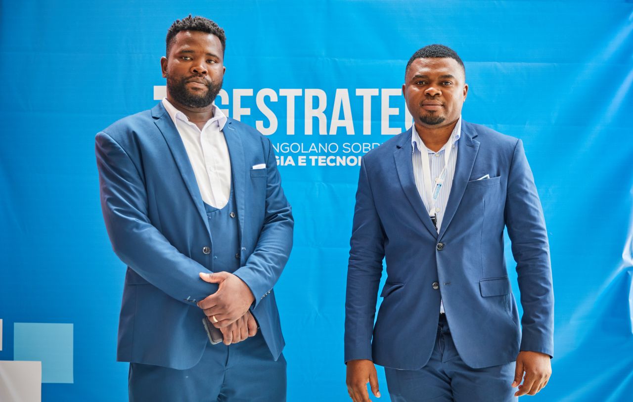 Services Two men in blue suits pose at a professional conference against a branded backdrop.