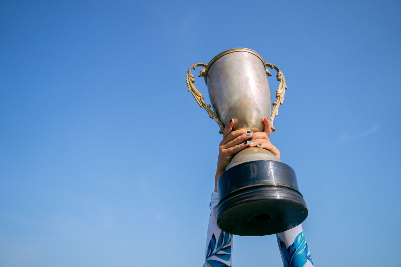Services Hands holding a trophy high against a clear blue sky, symbolizing victory and success.