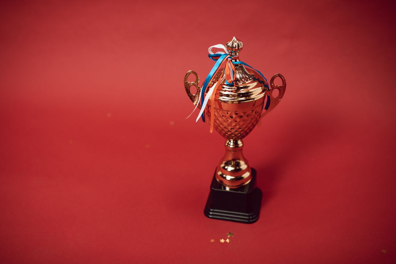 Mastering the First Impression: Your intriguing post title goes here Golden trophy cup with red, blue, and white ribbons on a red backdrop symbolizes achievement and success.