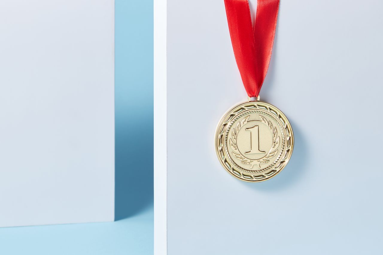 Home Close-up of a gold medal with a red ribbon hanging against a light blue background.